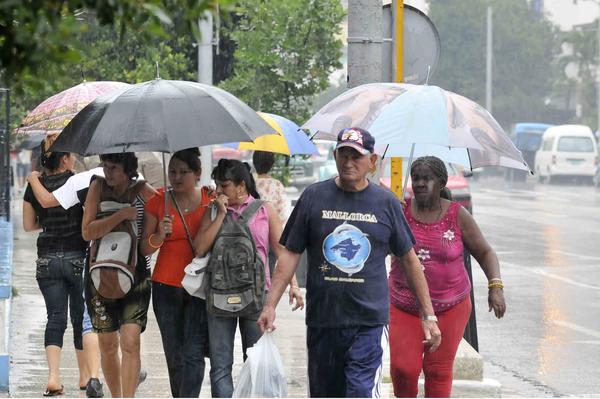 Transeúntes caminan por la calle 23 protegidos por sombrillas bajo las intensas lluvias que azotan La Habana, Cuba, el 5 de junio de 2013. AIN FOTO/Roberto MOREJÓN RODRÍGUEZ