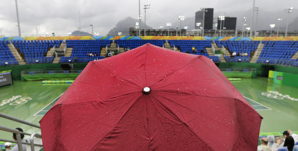 Fanáticos con paraguyas aguardan bajo la lluvia en la sede del tenis de los Juegos Olímpicos el miércoles, 10 de agosto de 2016, en Río de Janeiro. (AP Photo/Charles Krupa)
