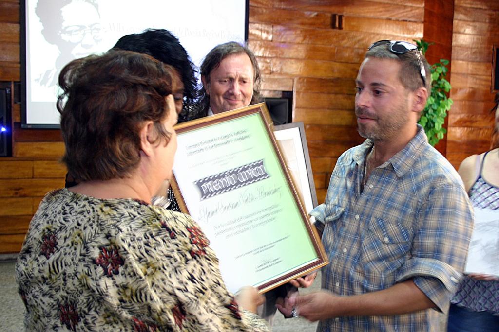 Alina Martínez Triay, subdirectora de Trabajadores, entrega el respectivo reconocimiento al ganador de este certamen, quien tambien recibió un lienzo de Erik Varela. Foto: César A. Rodríguez Rodríguez