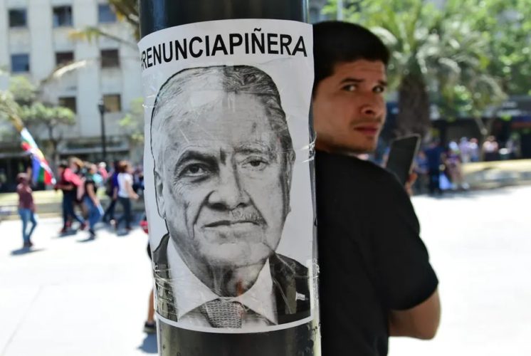 Los manifestantes en las calles han exigido la renuncia del actual presidente. En la foto, un joven exhibe montaje de los rostros del presidente Sebastián Piñera y del dictador Augusto Pinochet, con la leyenda “Renuncia Piñera”. Foto: Martin Bernetti/AFP