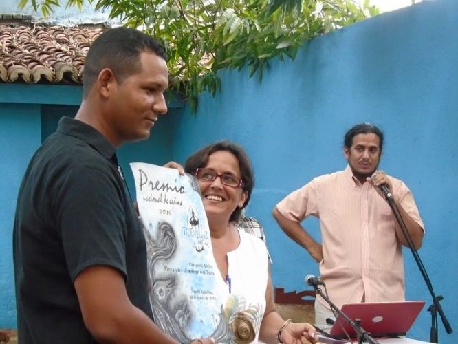 A la izquierda, Alexander, al recibir el Premio Toda luz y toda mía 2016 por su obra Colmillos de costa, de manos de Merari Mangly, presidenta de la agrupación decimista espirituana. Al fondo, Karel Leyva, integrante del jurado y vicepresidente del Grupo Ala Décima. Foto: Periódico Escambray.