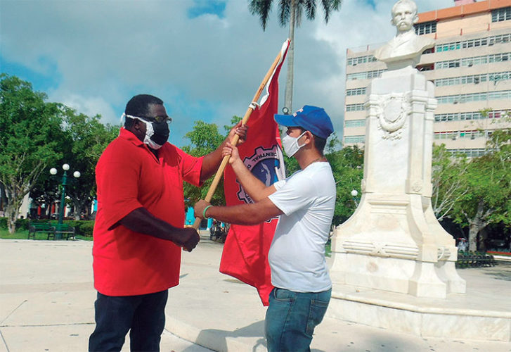 El joven sindicalista Roberto Gil Pérez, representante de la Brigada Lázaro Peña, recibe la bandera del colectivo de manos de Héctor Benítez, secretario general de la CTC en Ciego de Ávila. Foto: Pastor Batista Valdés